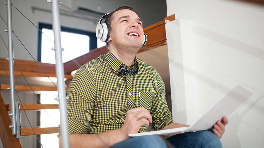 Man wearing headphones, sitting on steps with a laptop, smiling.