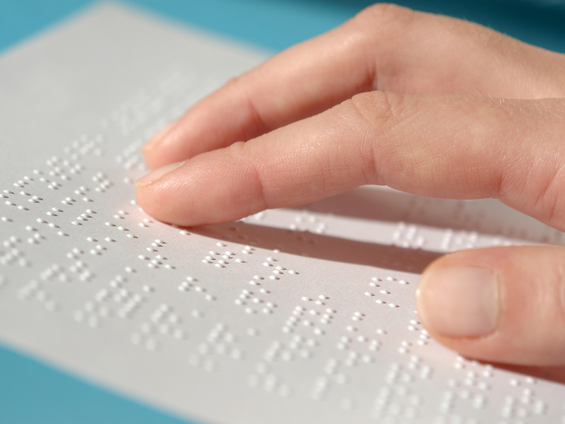 Image of a hand touching a sheet of embossed Braille
